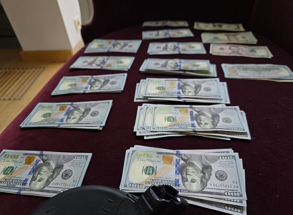 Przedmioty znalezione w przeszukiwanych mieszkaniach - rozłożone na stole banknoty po 100 dolarów
