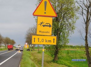 Znak drogowy z napisem wypadki w tle policjanci i pojazdy na miejscu wypadku