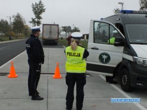 Policjant i policjantka stiją w trakcie kontroli na tle pojazdu inspekcji oraz pojazdu ciężarowego