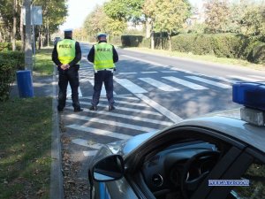 Dwaj policjanci pełnią służbę w rejonie przejścia dla pieszych na ulicy.