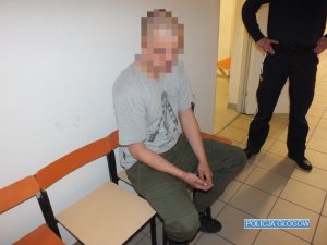 Podejrzany siedzi na krześle obok niego stoi policjant