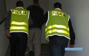 Policjanci w kamizelkach prowadzą zatrzymanego po schodach