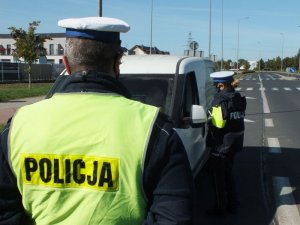 Policjanci z ruchu drogowego podczas działań pieszy kontra pojazd. Policjanci stoją przy samochodzie ubrani w kamizelki odblaskowe.