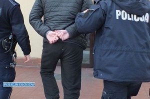 Policjanci prowadzą zatrzymanego mężczyznę, który ma założone kajdanki na ręce trzymane z tyłu